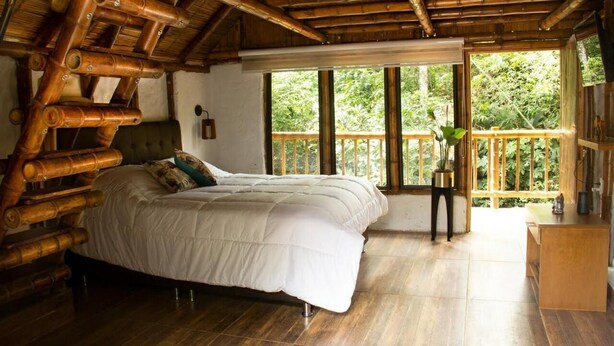 Una habitación con una cama grande, vigas de madera en el techo y un balcón con vistas al verdor.