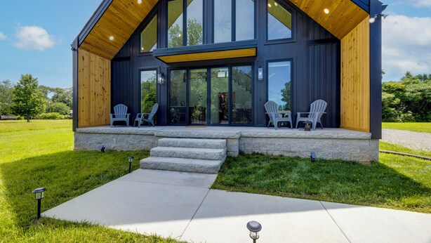 Una casa moderna con un amplio porche, escalones de piedra y dos sillas Adirondack.