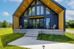 Una casa moderna con un amplio porche, escalones de piedra y dos sillas Adirondack.