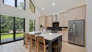 Una cocina moderna con una isla grande, sillas de madera y vistas a un paisaje verde.