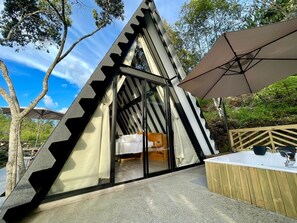 Una tenda a forma triangolare con un letto all'interno, una panca di legno e un ombrellone grande.
