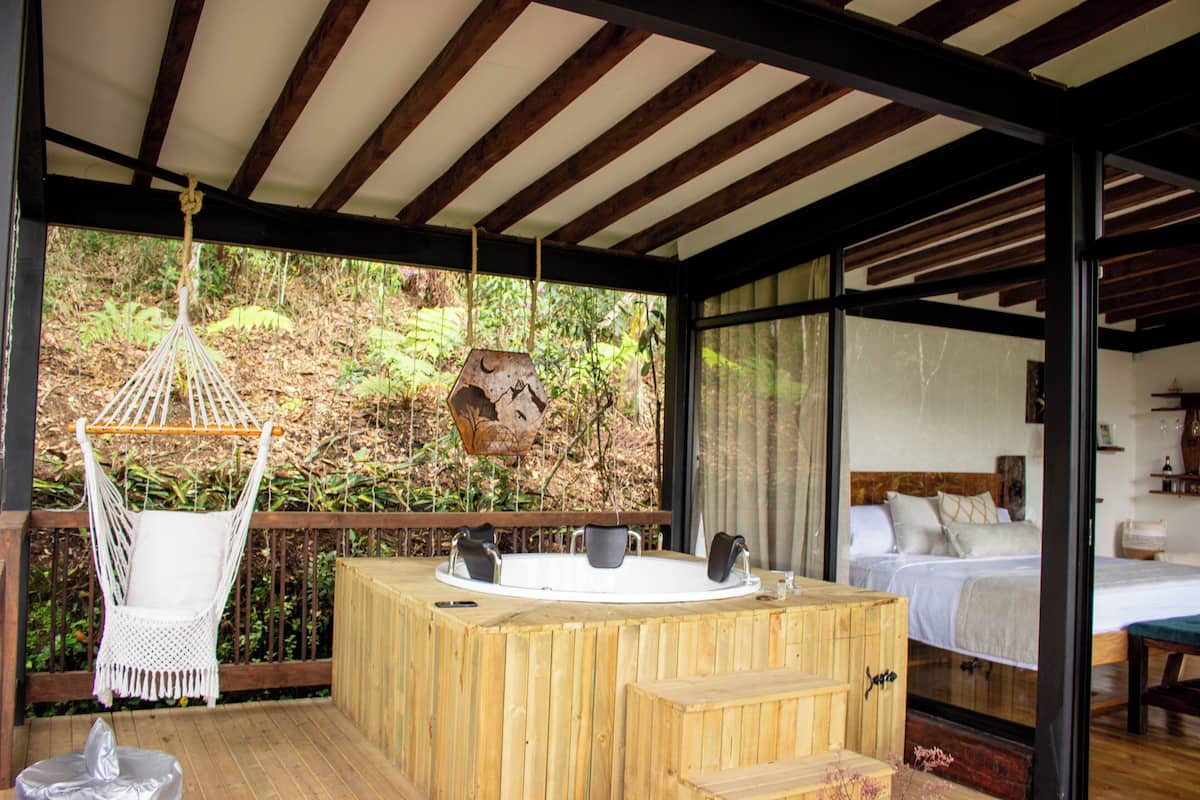 A wooden deck with a hot tub, a hanging chair, and a bed with a wooden headboard.