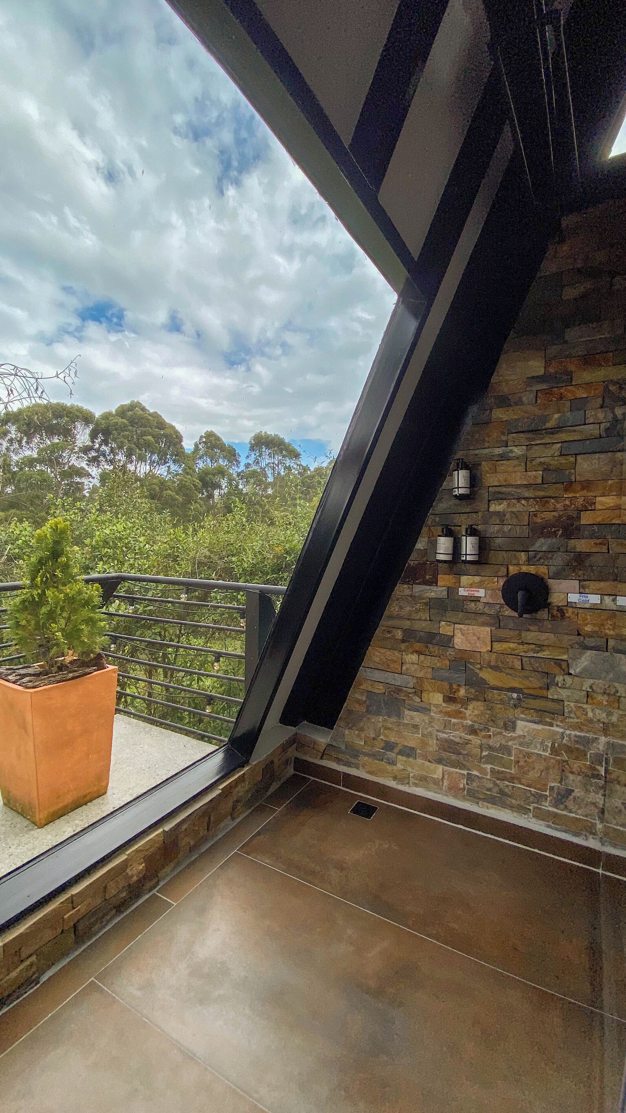 A balcony with a stone wall, a potted plant, and a view of trees and sky.
