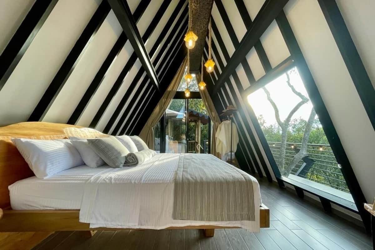 A bedroom with a sloped ceiling, wooden beams, and a bed with white bedding.