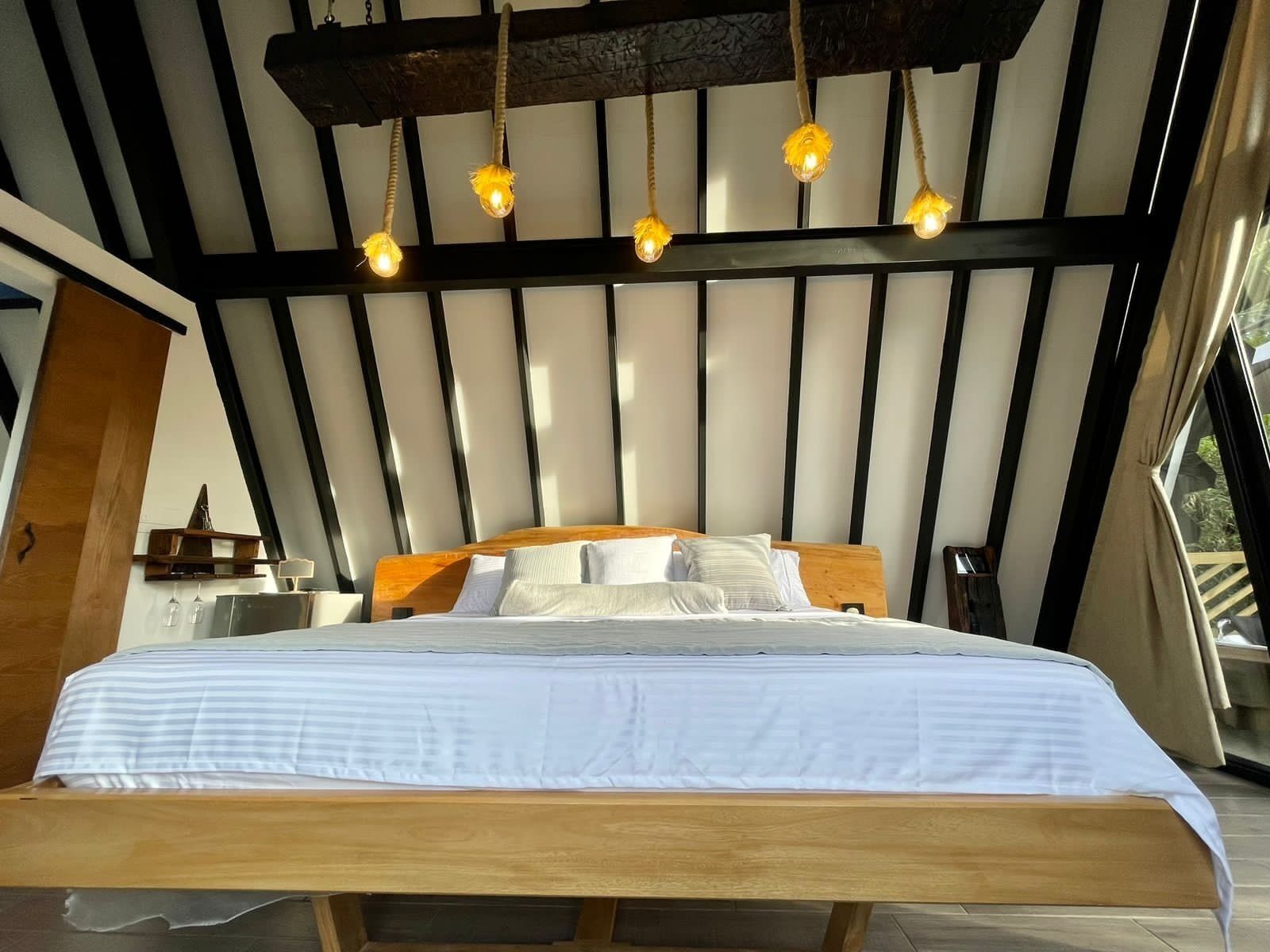 A bedroom with a wooden bed, white bedding, a wooden headboard, and a ceiling with hanging lights.