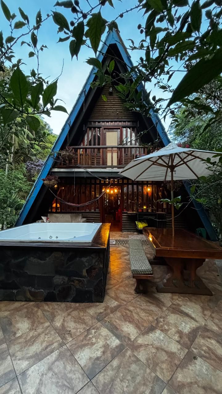 A triangular wooden building with a balcony, stone flooring, and an umbrella.