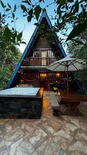 A triangular wooden building with a balcony, stone flooring, and an umbrella. - Ecoluxury glamping (El Carmen de Viboral)