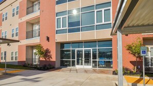 A multi-story building with a glass entrance, brick facade, and a wheelchair-accessible parking sign.