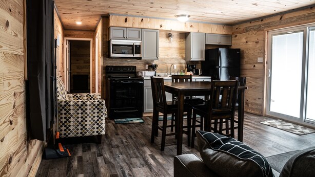 A compact kitchen with wooden walls, a dining area, and a large sliding glass door to the right.