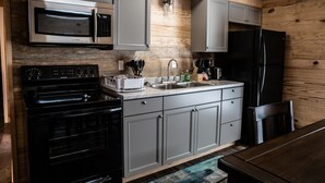 A modern kitchen with grey cabinets, a black stove, a stainless steel microwave, and a black refrigerator.
