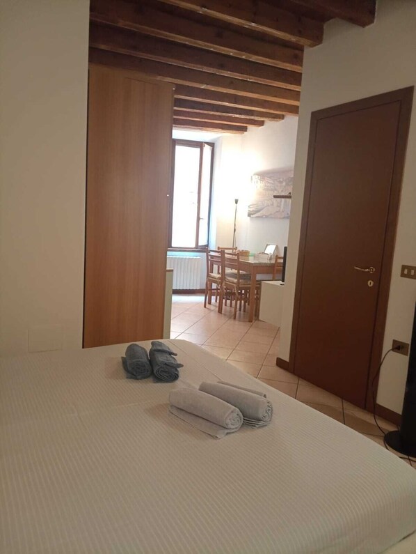 A hotel room with a bed, a wooden door, and a view of a dining area with a table and chairs.