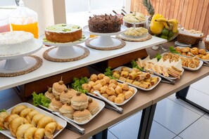 A buffet table with various food items including cakes, sandwiches, and pastries. - Hanna Praia Hotel (Florianópolis)