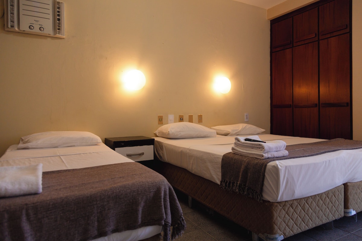A hotel room with two beds, each with white linens and a brown blanket. There is a wooden wardrobe and a wall-mounted air conditioning unit.