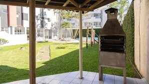 Ένας εξωτερικός χώρος με αίθριο, ψησταριά, πλακάκια στο δάπεδο και θέα σε ένα οικιστικό κτίριο στο βάθος.