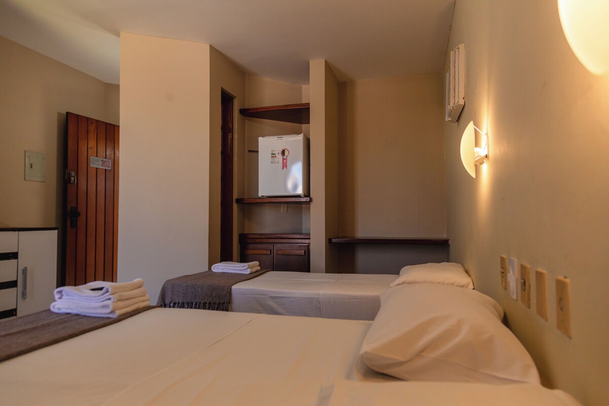 Habitación de hotel con dos camas, una puerta de madera, un refrigerador y una lámpara fijada a la pared.