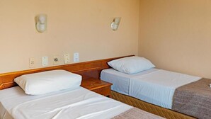 Une chambre d’hôtel avec deux lits simples, une tête de lit en bois, des tables de chevet et des appliques murales.