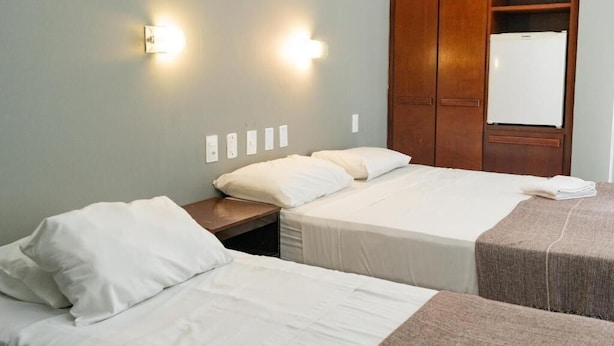 Une chambre d’hôtel avec deux lits, une armoire en bois et un réfrigérateur blanc.