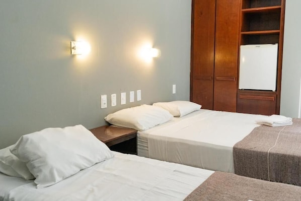 A hotel room with two beds, a wooden wardrobe, and a white refrigerator. - Hanna Praia Hotel (Florianópolis)