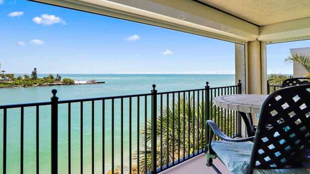 A balcony with a view of the ocean, a table, and chairs.
