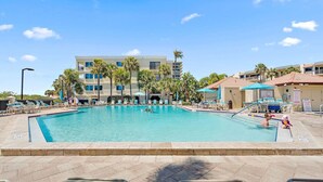 A swimming pool with lounge chairs, palm trees, and a building with balconies in the background.