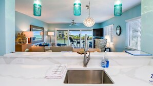 A modern kitchen with a large island, stainless steel sink, and pendant lights.