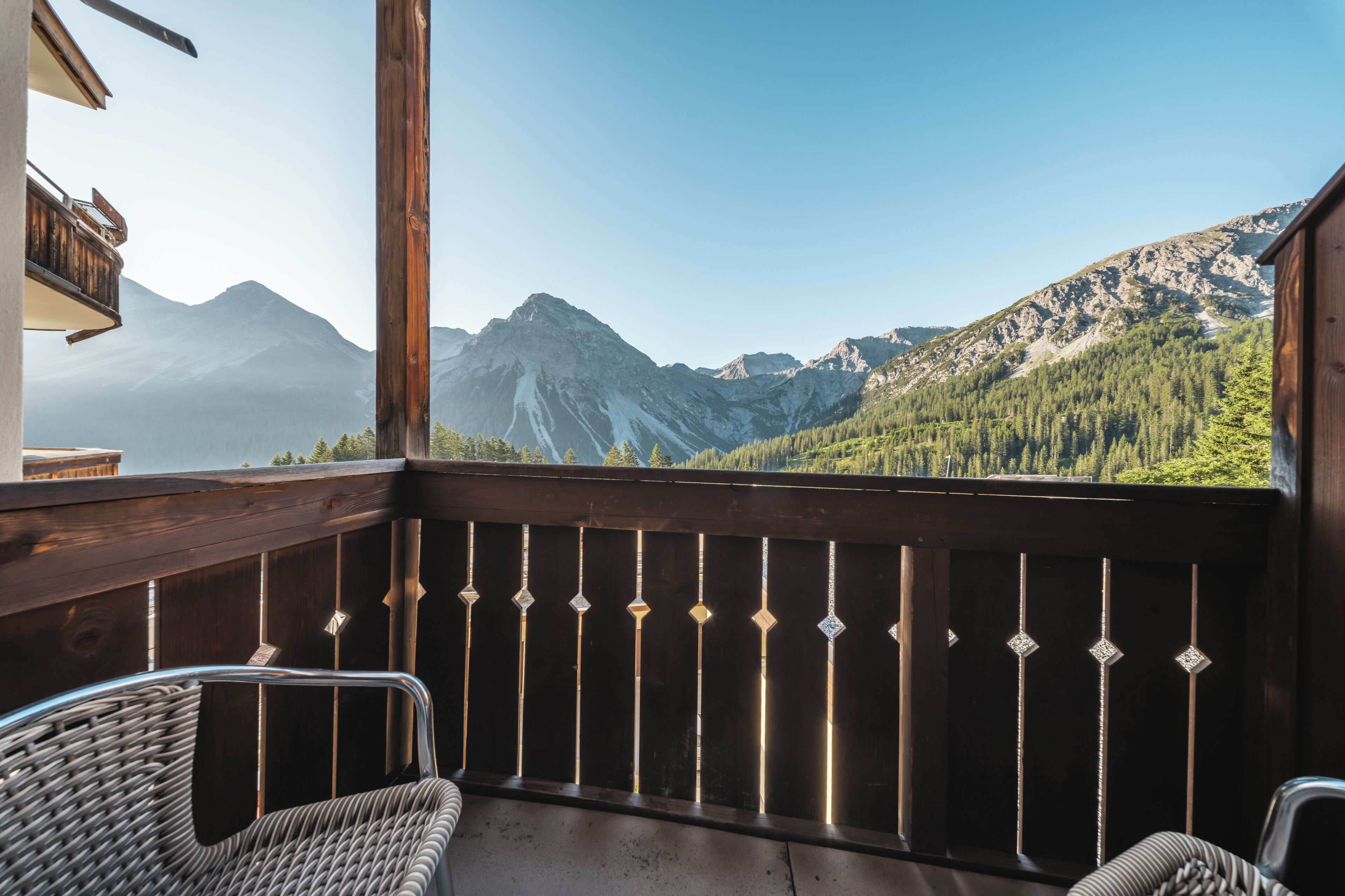 A balcony with wicker chairs, a wooden railing, and a mountain view.
