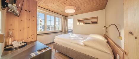 A bedroom with a wooden ceiling, a bed with white bedding, a bedside table with a lamp, and a window with curtains.