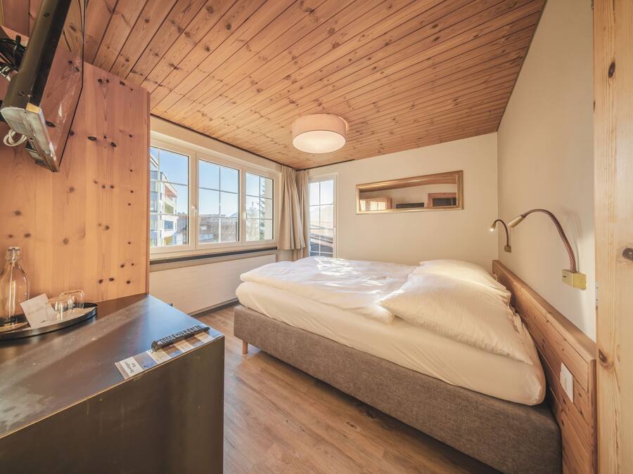 Une chambre avec un plafond en bois, un lit avec une literie blanche, une table de chevet avec une lampe et une fenêtre avec des rideaux.