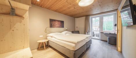 A modern bedroom with a wooden ceiling, a large bed, a small stool, and a window with a view of the outdoors.