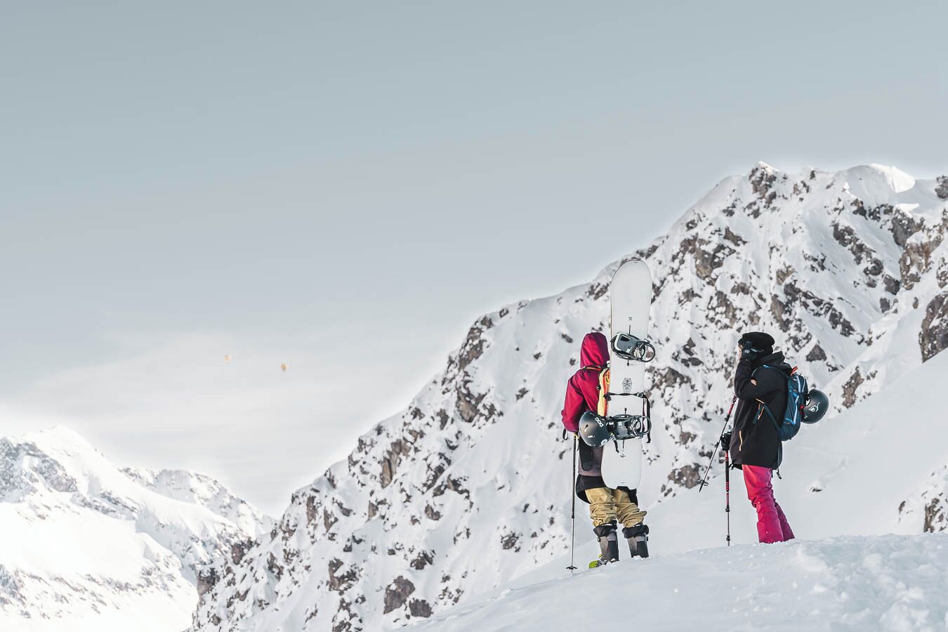 Deux personnes se tiennent debout sur une montagne enneigée, sous un ciel dégagé.