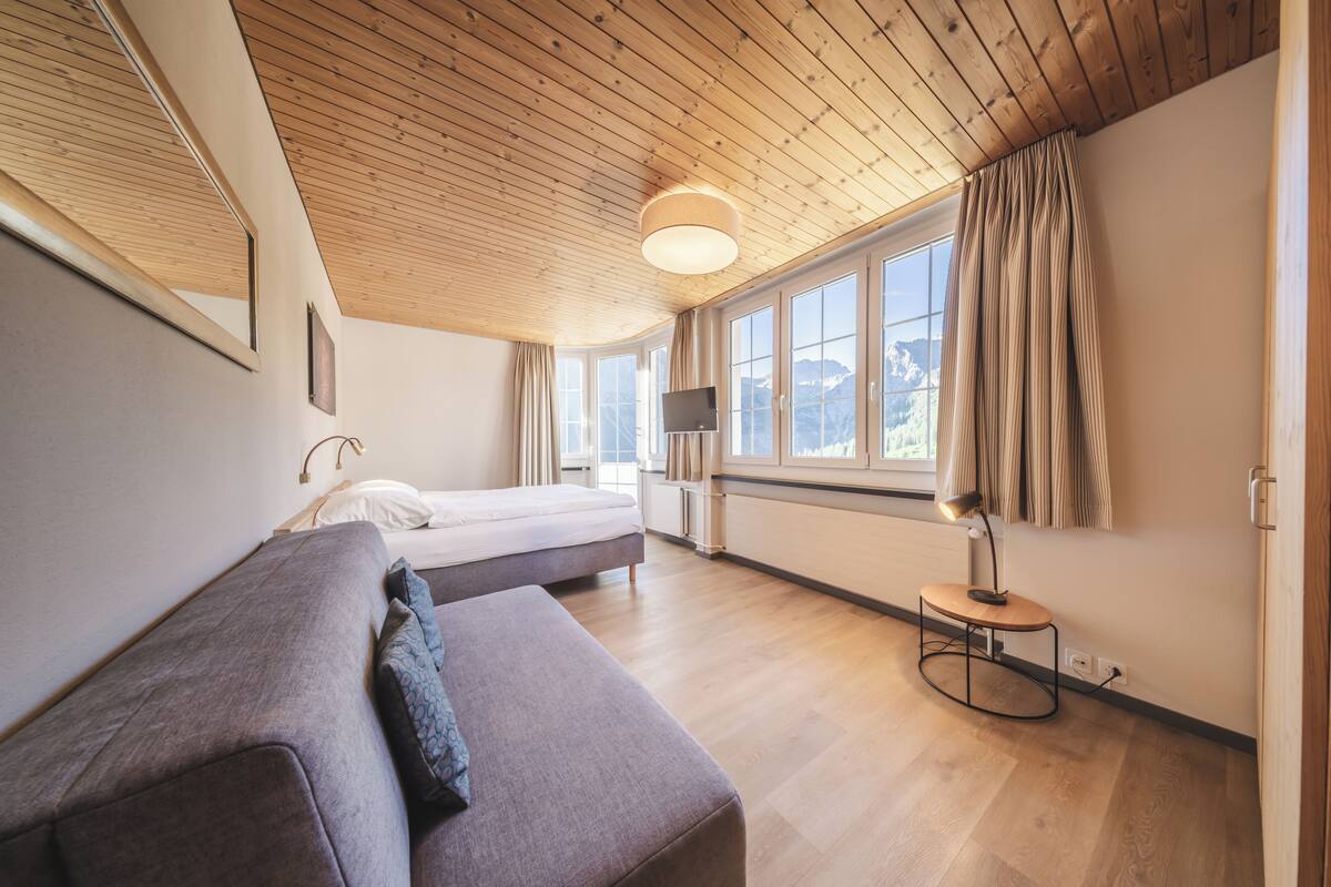 Quarto moderno com teto de madeira, uma cama, um sofá, uma TV e uma janela com cortinas.