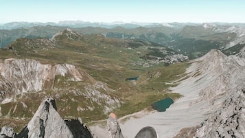 A person's foot on a mountain peak overlooking a valley with a lake and distant mountains.