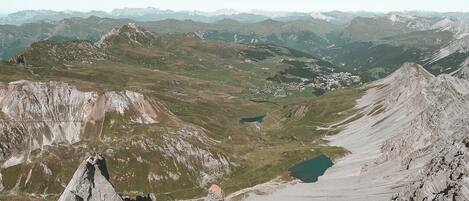 A person's foot on a mountain peak overlooking a valley with a lake and distant mountains.