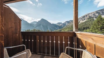 Un balcon en bois agrémenté de chaises en osier, offrant une vue sur les montagnes et la forêt.