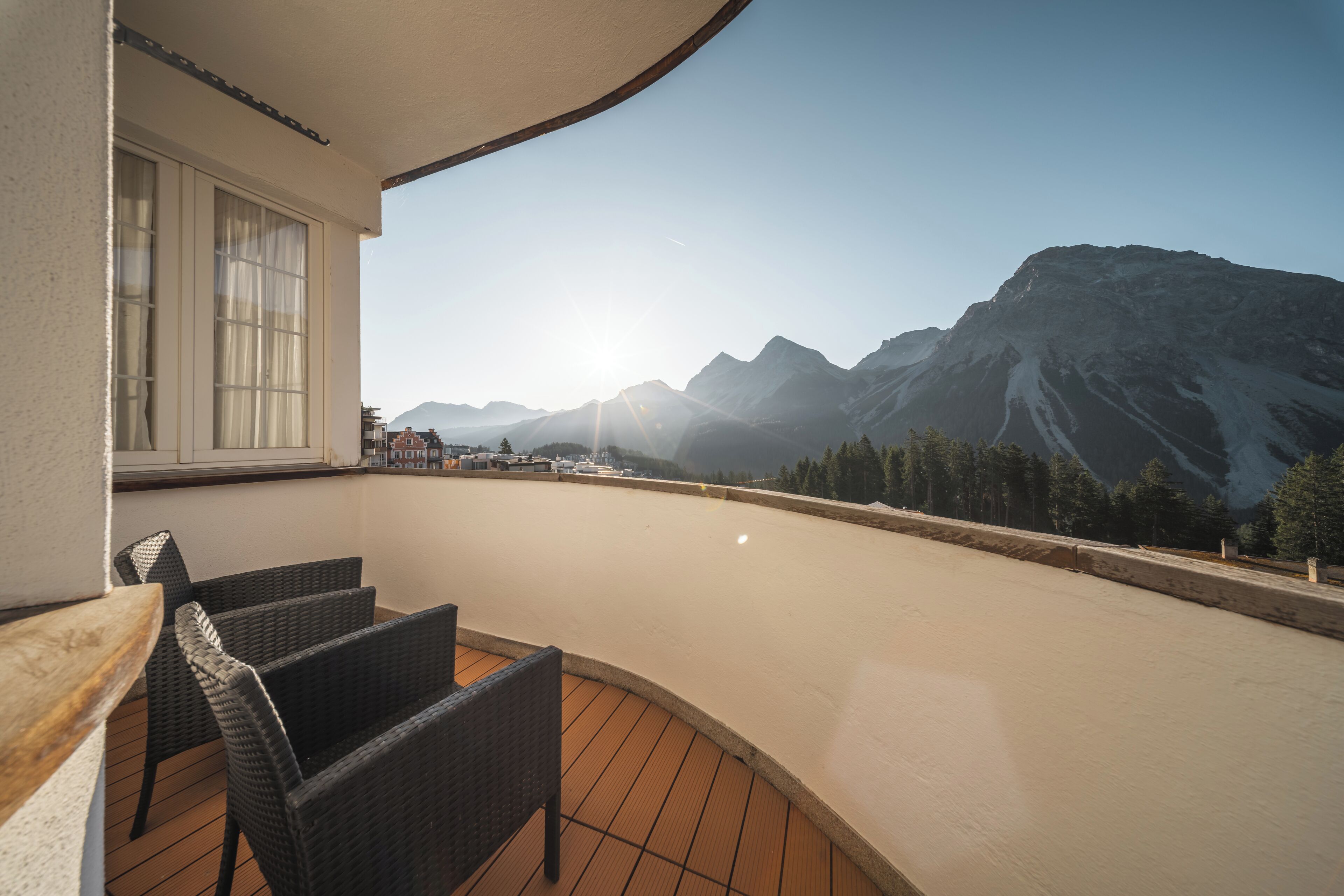 A balcony with wicker chairs, a wooden table, and a view of mountains.