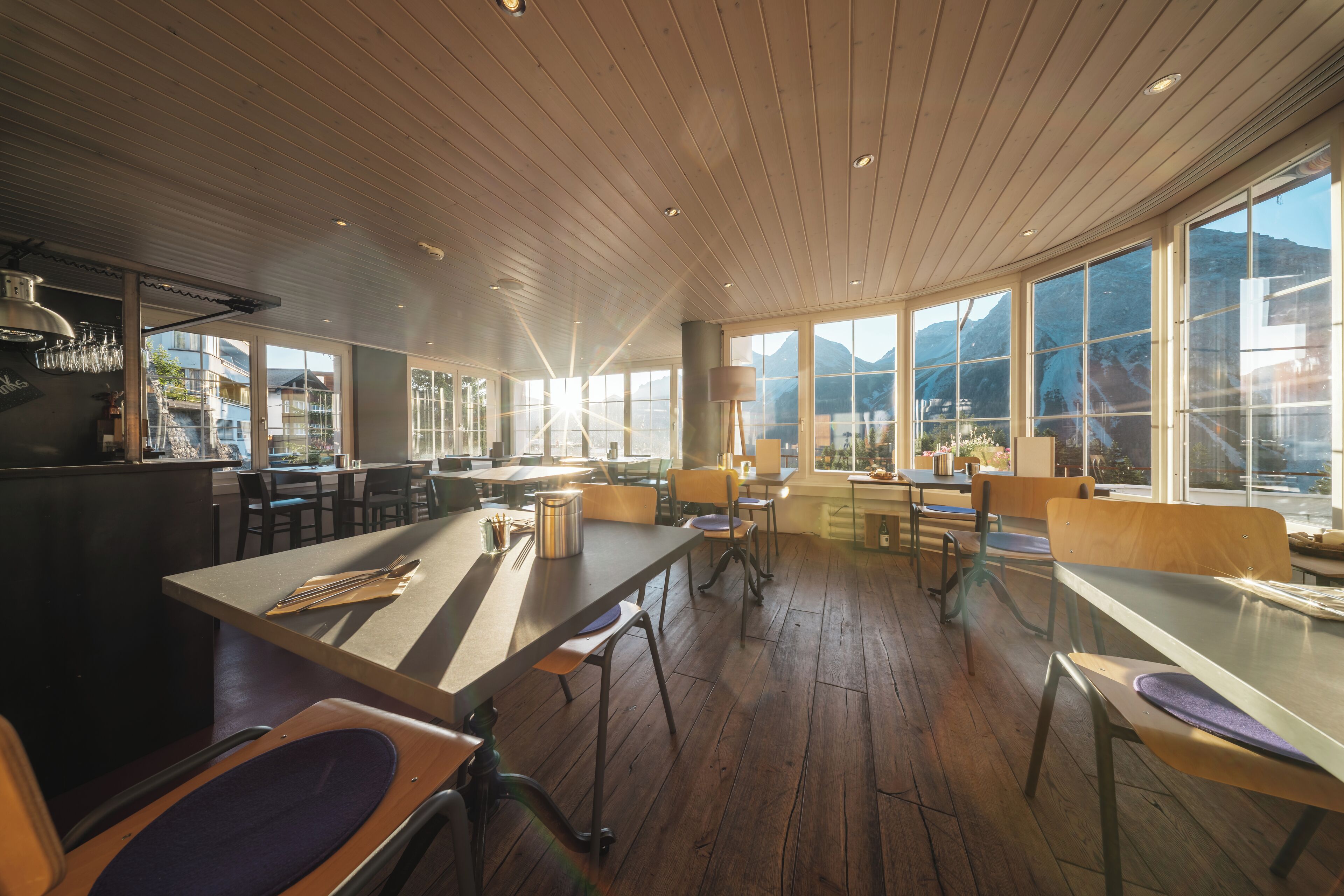 Un ristorante moderno con pavimenti in legno, ampie finestre e un'area bar centrale.