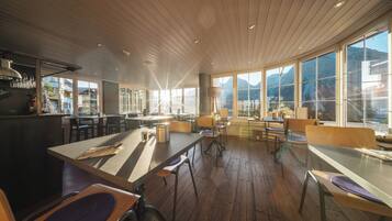 A modern restaurant with wooden floors, large windows, and a central bar area.