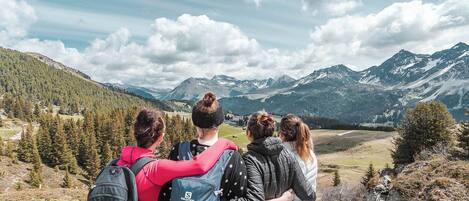 A group of people standing on a mountain trail with a view of a valley and mountains in the background.