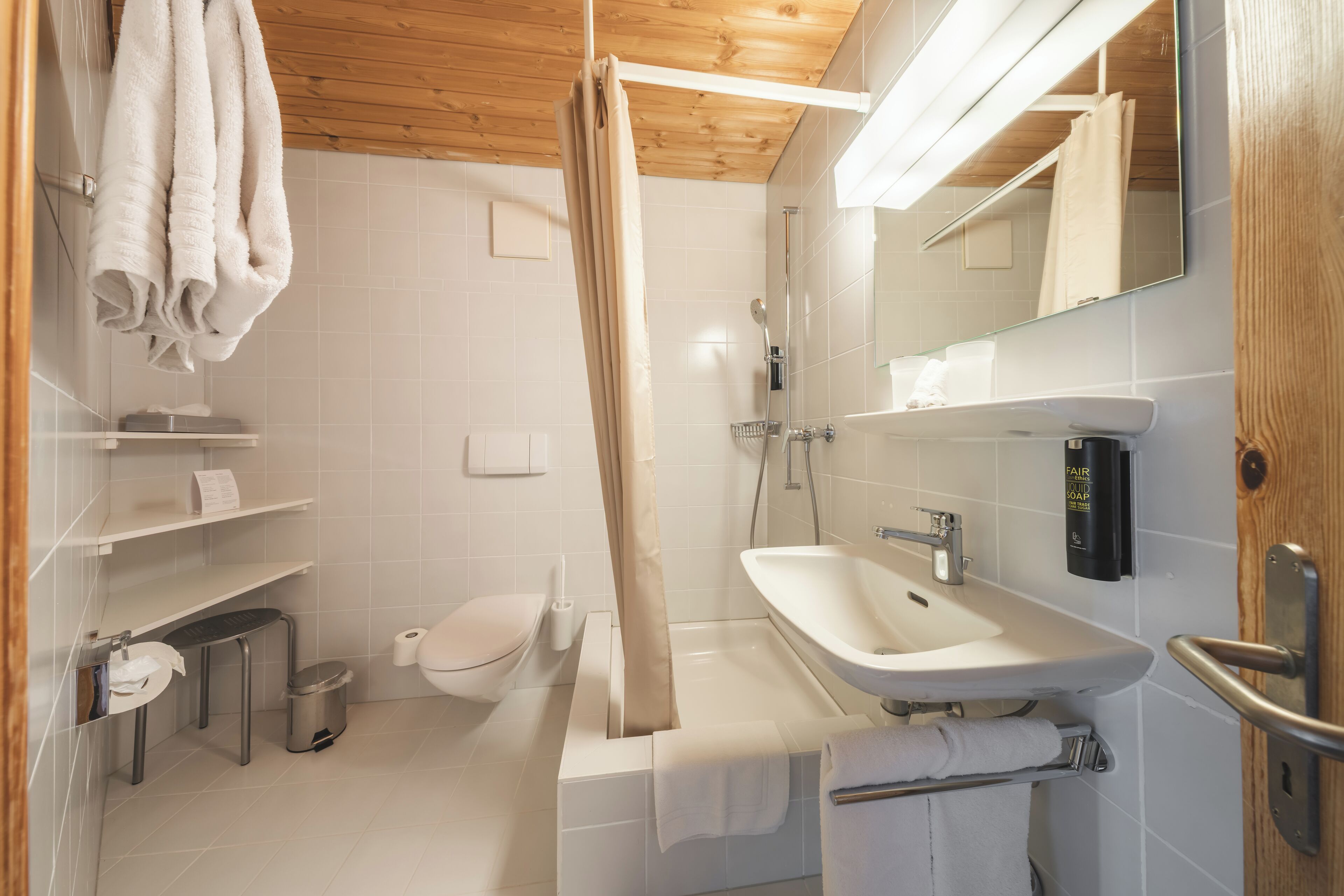 A modern bathroom with a wooden ceiling, white tiles, a sink, a toilet, and a shower curtain.