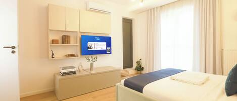 Una habitación de hotel moderna con cama, escritorio, televisor y ventana con cortinas.