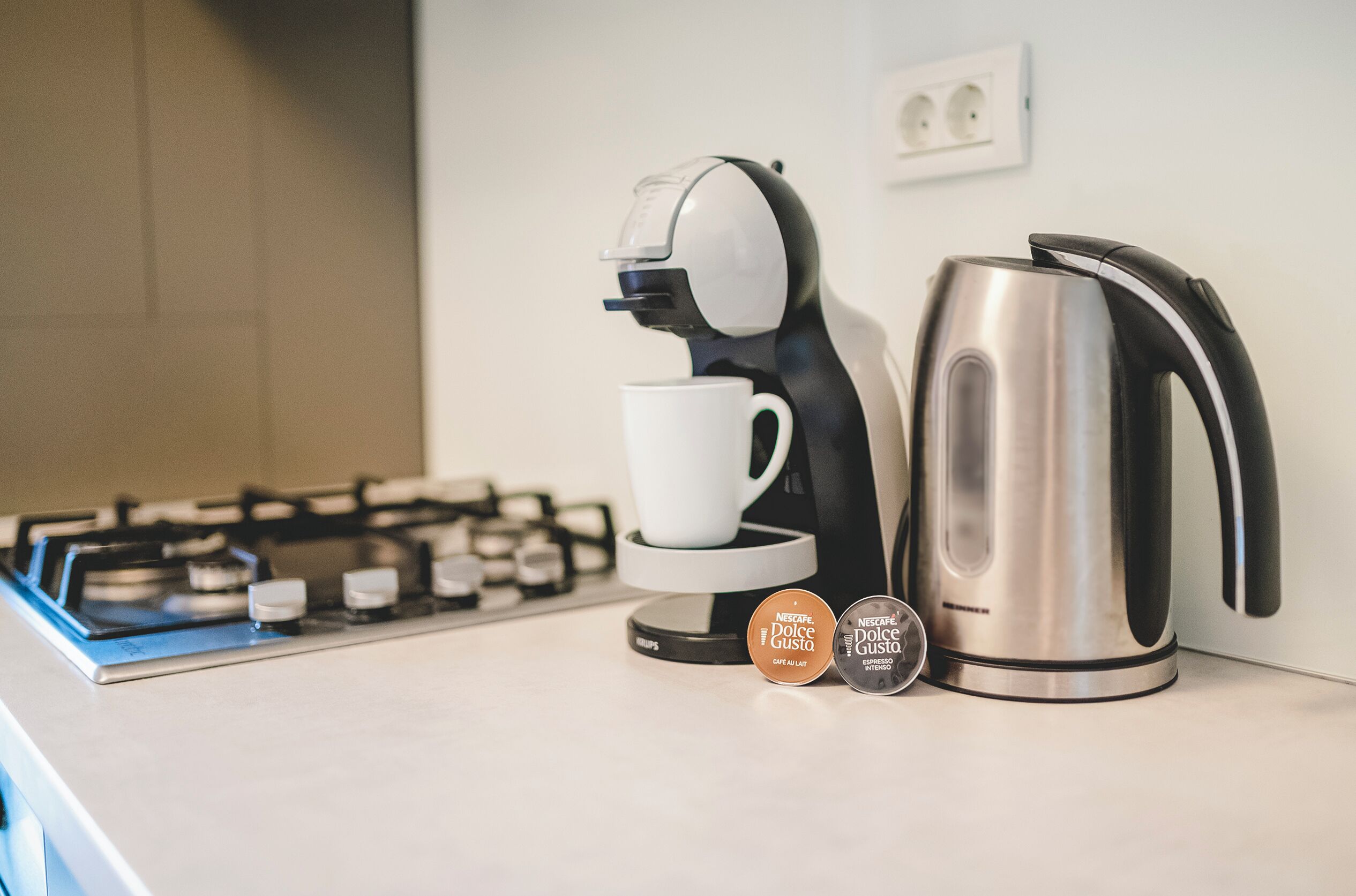 A kitchen with a coffee maker, a kettle, and a coffee pod on the counter.