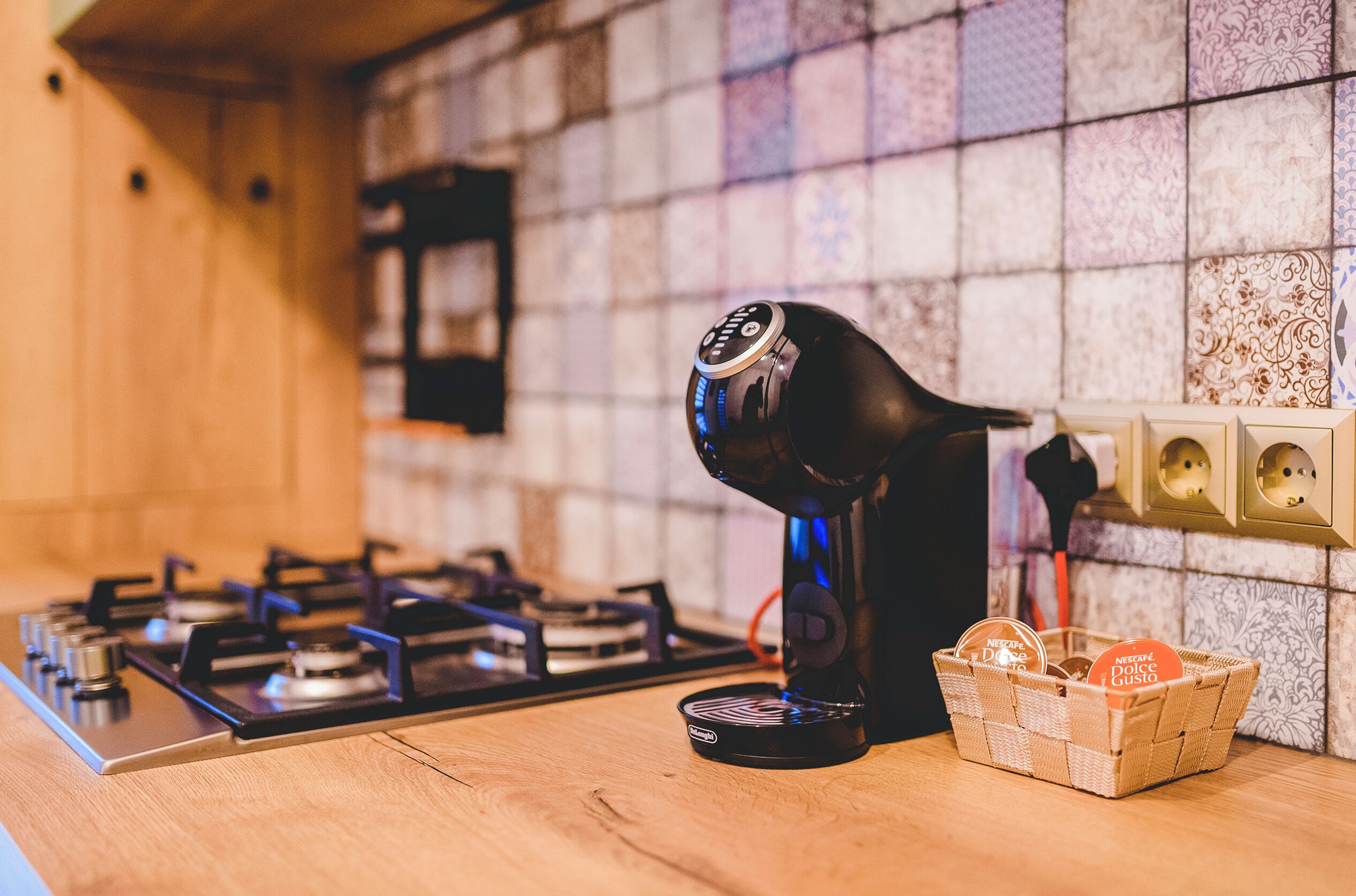 A kitchen with a gas stove, a coffee maker, and a basket of biscotti.