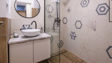 Un baño moderno con un lavamanos, espejo y ducha blancos.