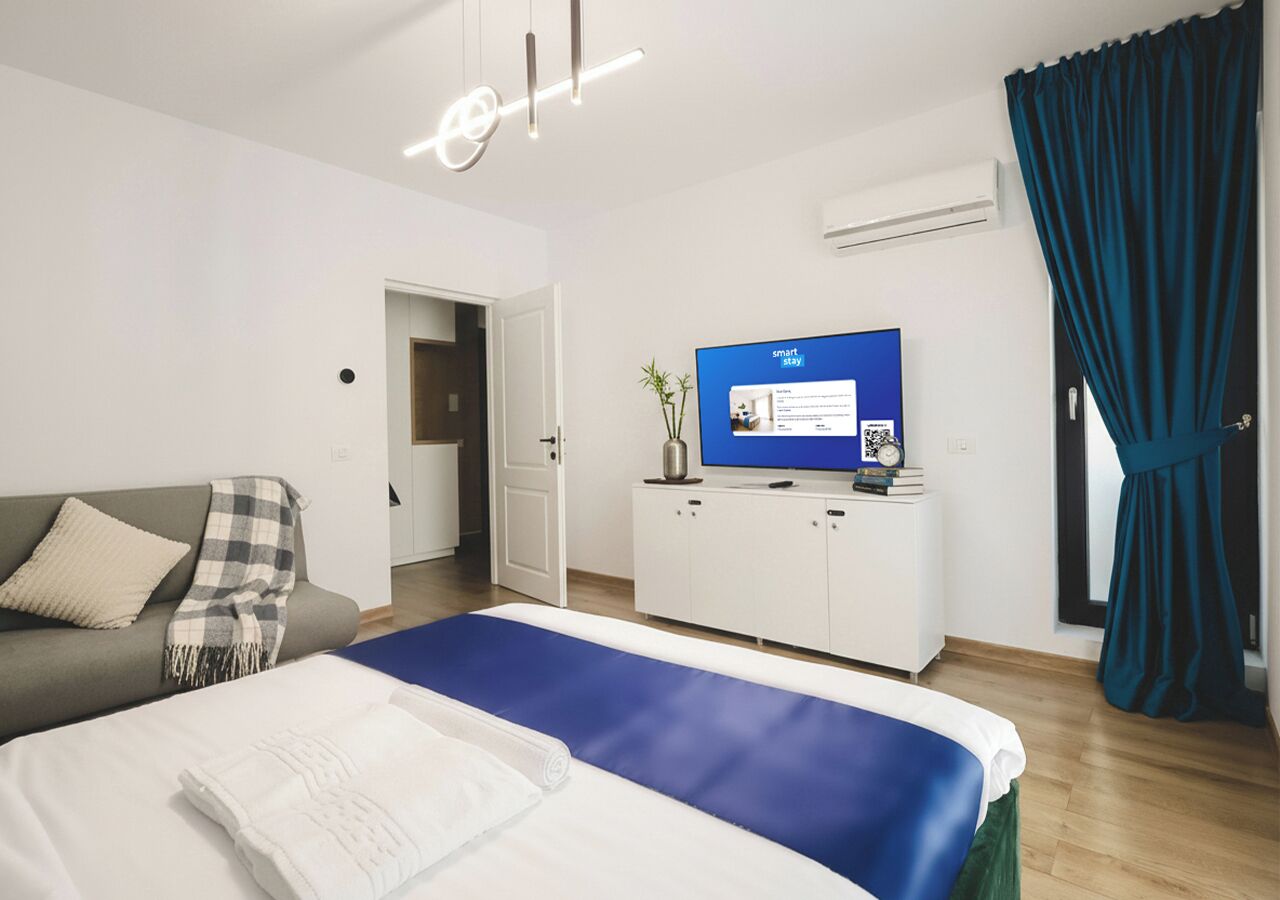 A modern hotel room with a bed, a sofa, a TV, and a desk.