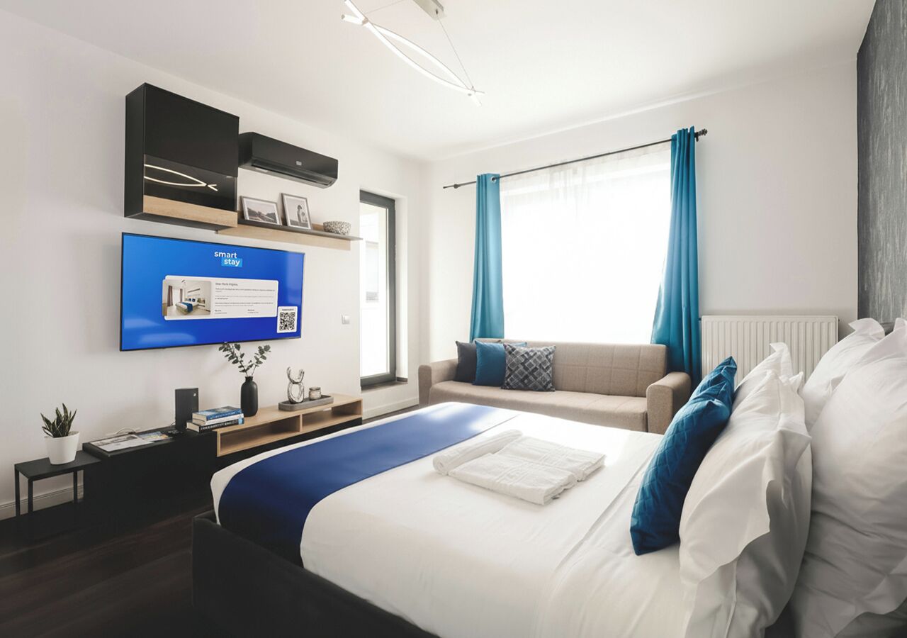 Een moderne hotelkamer met een groot bed, een flatscreen-tv, een bank en een raam met gordijnen.