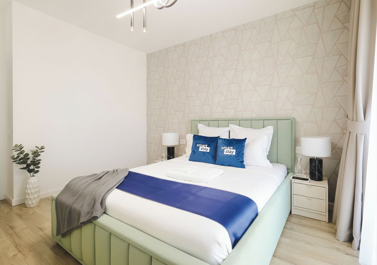 A modern hotel room with a bed, nightstands, a lamp, and a plant.