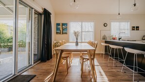 A modern kitchen with a dining area, large windows, and a view of greenery outside. - Cow Bell Cottage, quaint country retreat in Trentham (Trentham)