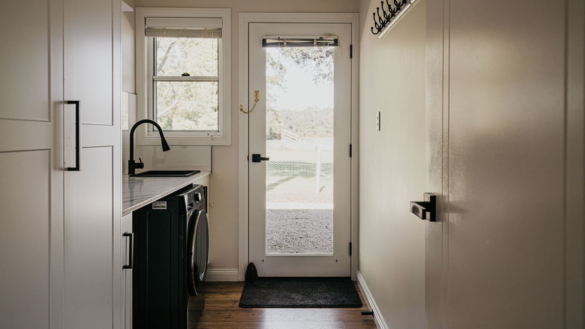 A narrow hallway with a kitchen area on the left, a washing machine, and a door leading to an outdoor area.