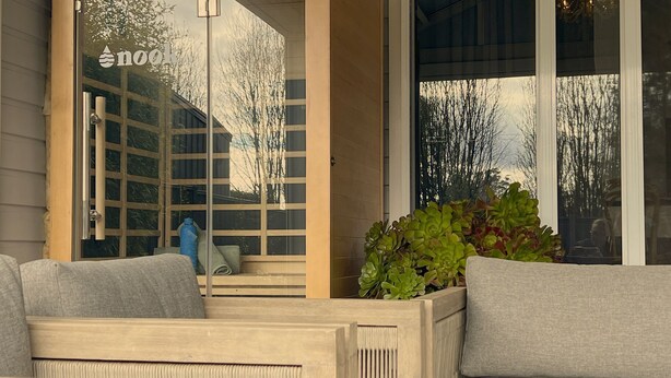 A wooden bench with cushions, a glass door with a reflection, and a planter with green plants. - Cow Bell Cottage, quaint country retreat in Trentham (Trentham)