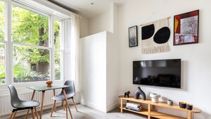 Una sala de estar moderna con un ventanal grande, una zona de comedor con sillas, un televisor y una estantería.
